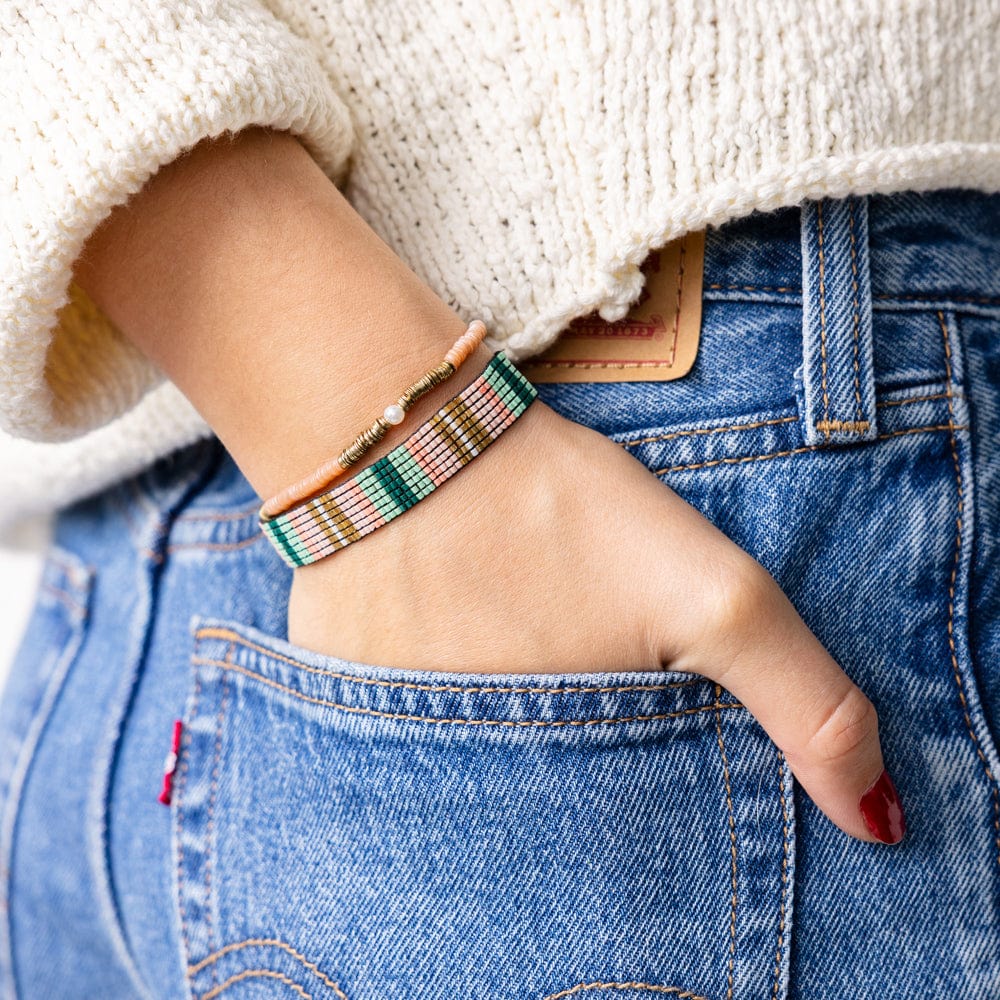 person wearing jeans and a green, blush, and gold beaded bracelet