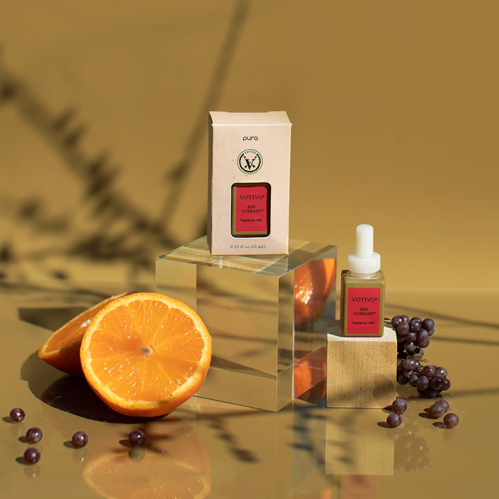 Red Currant Pura Fragrance Refill on a block of wood with its box packaging arranged with berries and sliced oranges.