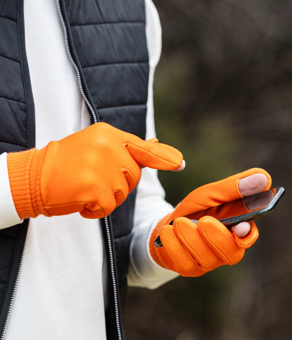 Person wearing orange gloves holding a phone with a blurred outdoor background
