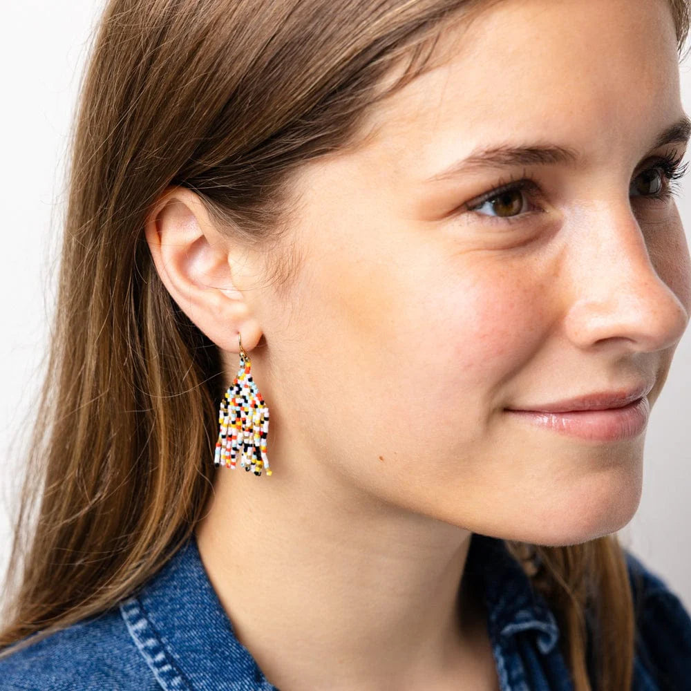 Close-up of a person wearing colorful tassel earrings with a neutral background
