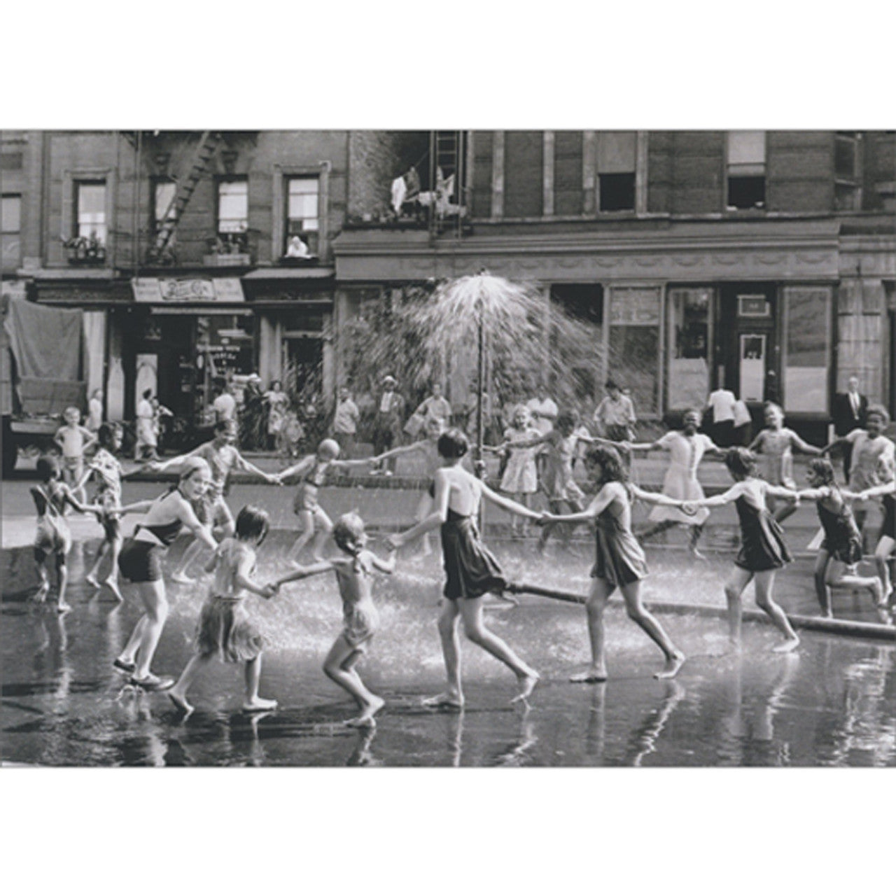 front of card is children holding hands in a large circle dancing around a sprinkler in black and white