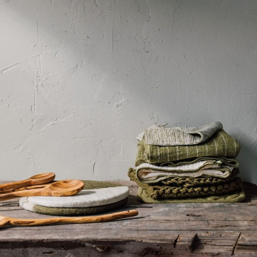 stack of folded towels and trivets set on a wooden table with wooden spoons.