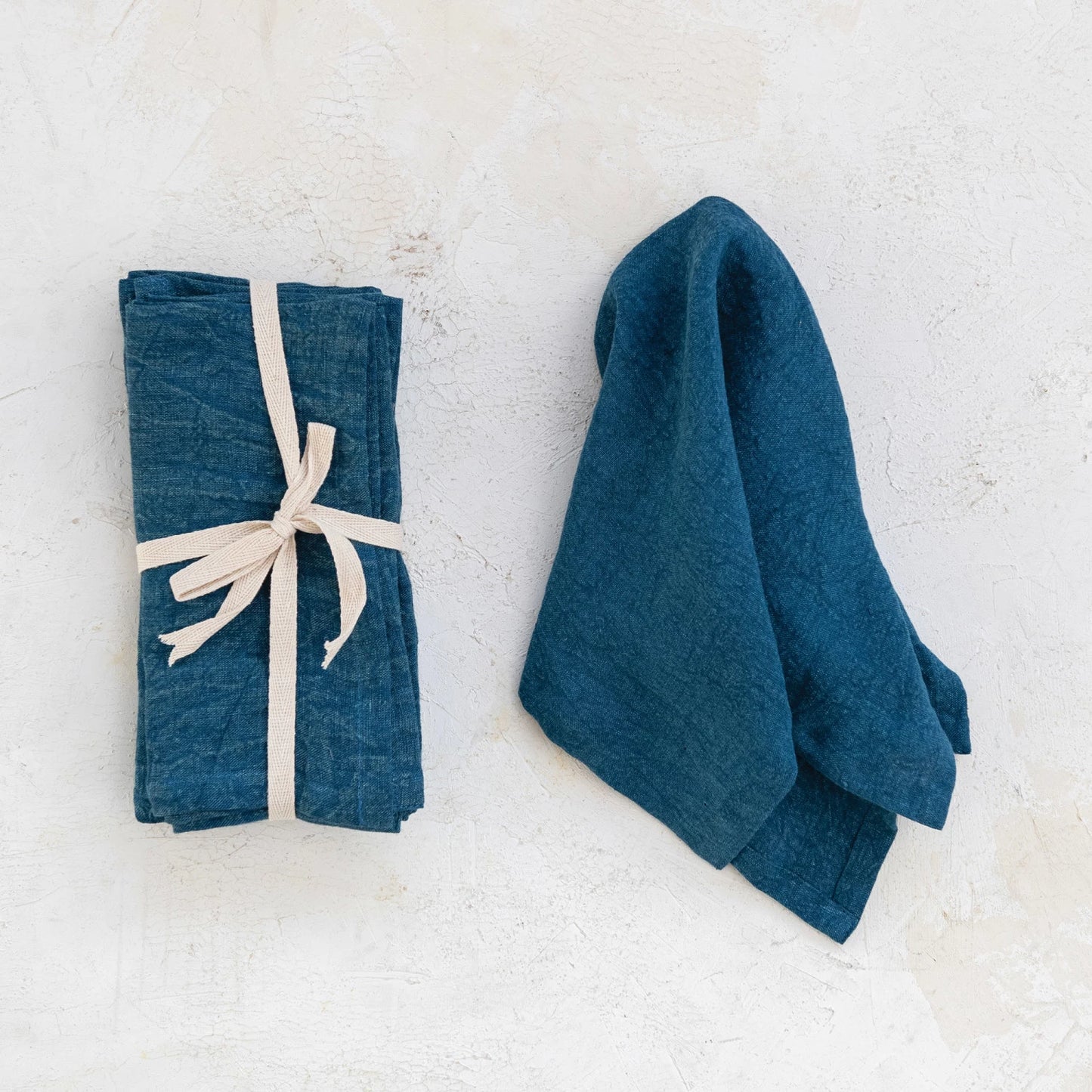 navy linen napkin draped next to a stack of navy napkins tied with a ribbon.