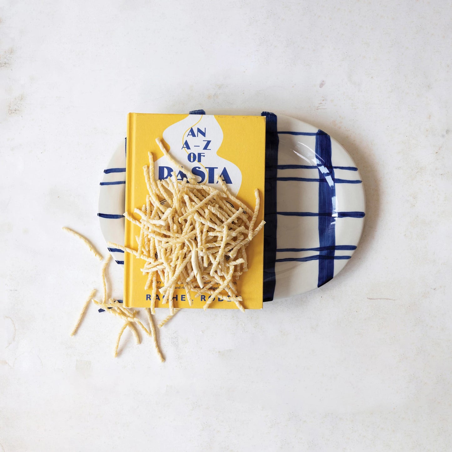 white and blue platter with a book about pasta and uncooked pasta set on it on a table.