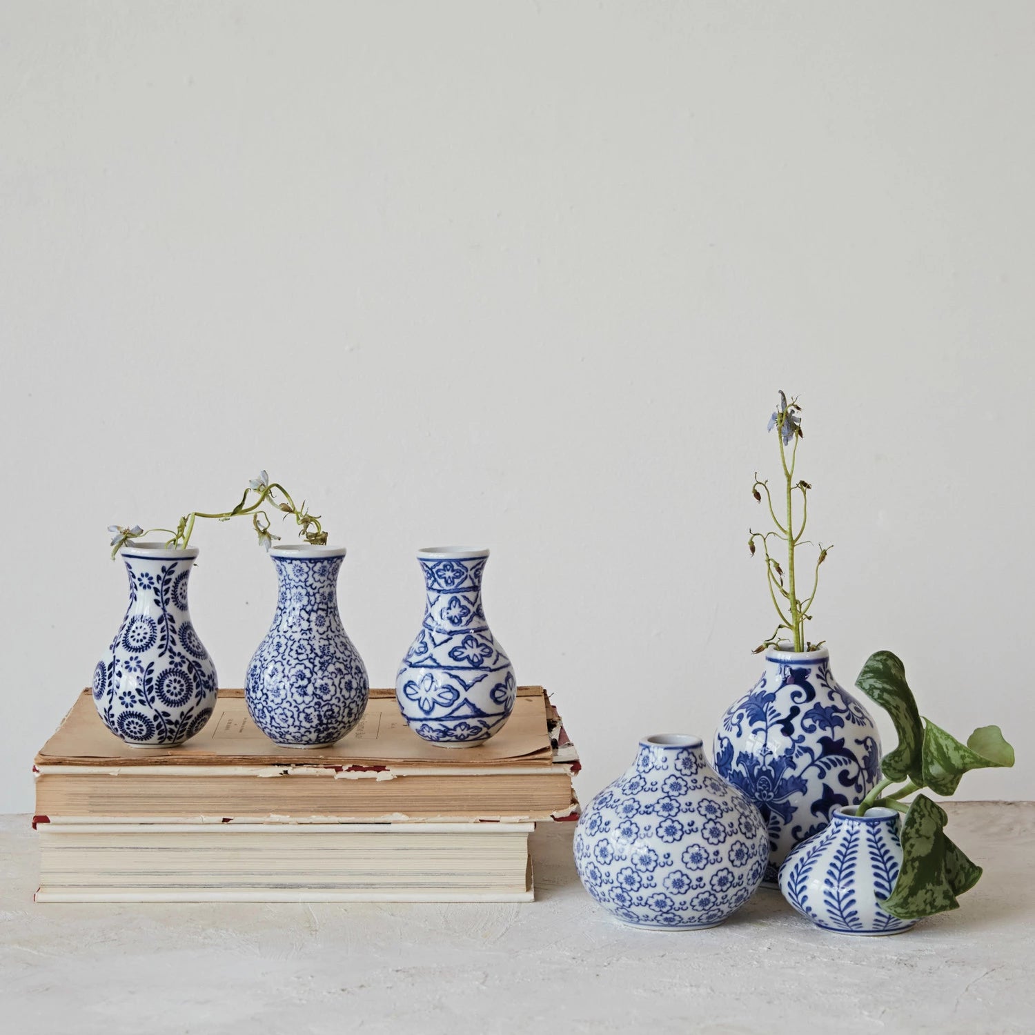 assorted blue and white patterned vases arranged on a shelf with books and greenery.