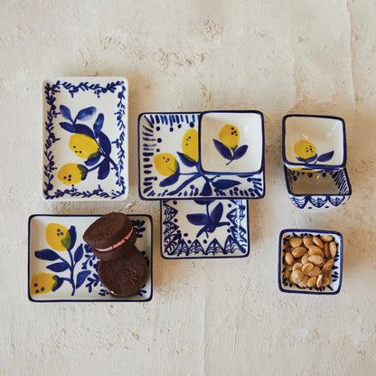 assorted sizes and style of blue and white dishes with lemons painted on them arranged on a plaster surface with nuts and cookies.