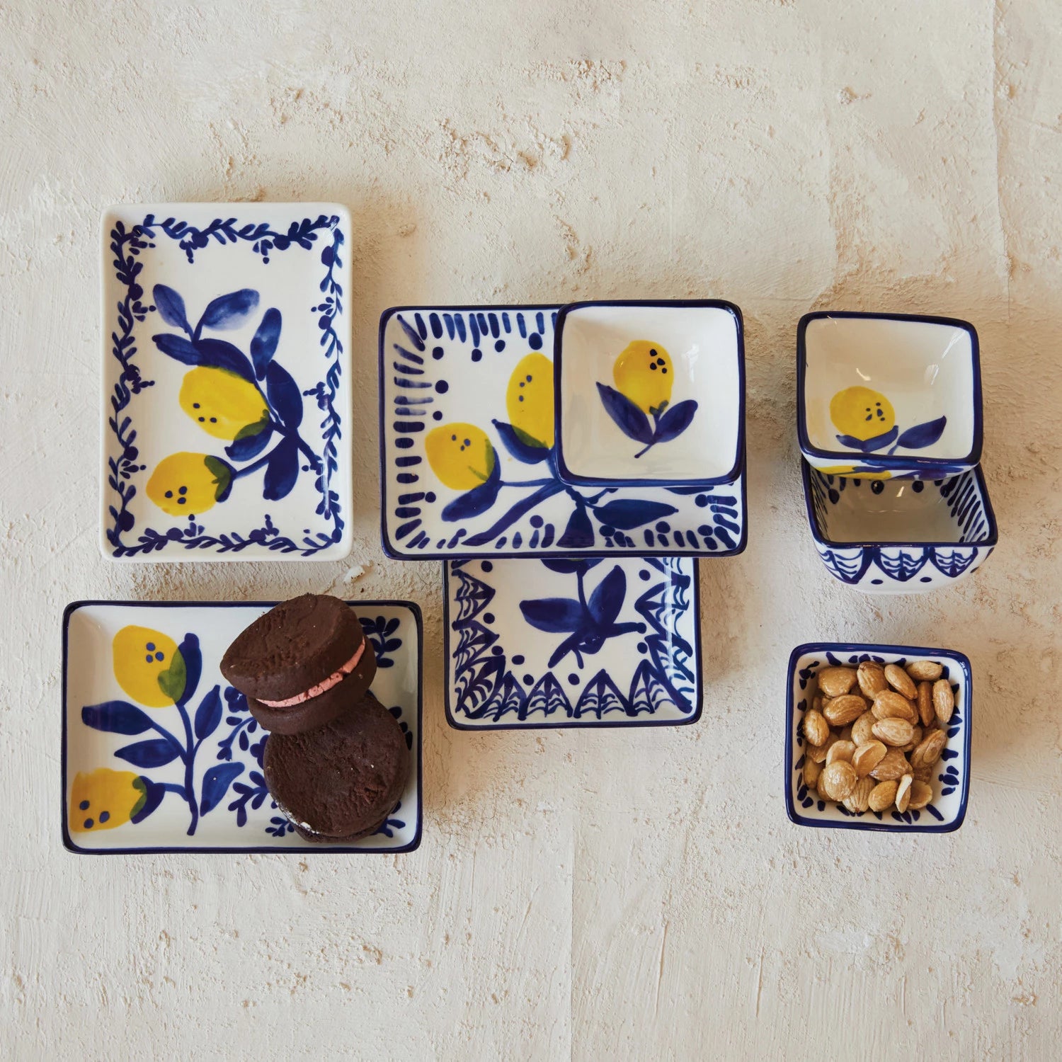 assorted blue and white dishes with lemon design arranged on a plaster surface, on eis filled with nuts, another has cookies on it.