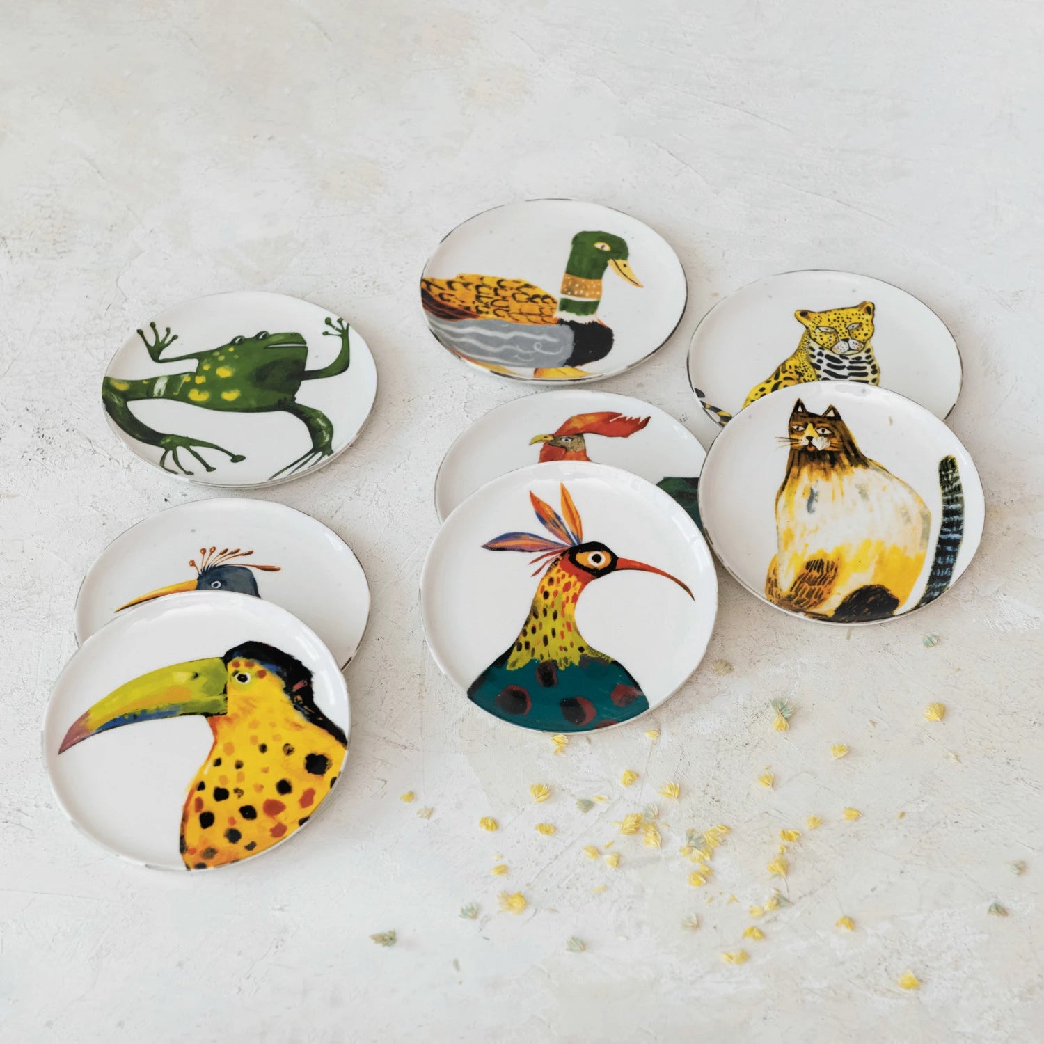 8 assorted plates with animal or bird artwork on them arranged on a plaster surface.