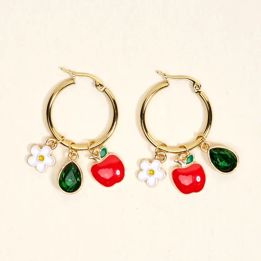 Gold hoop earrings with red apples, green leaves, and white flowers hanging on them shown on a beige background