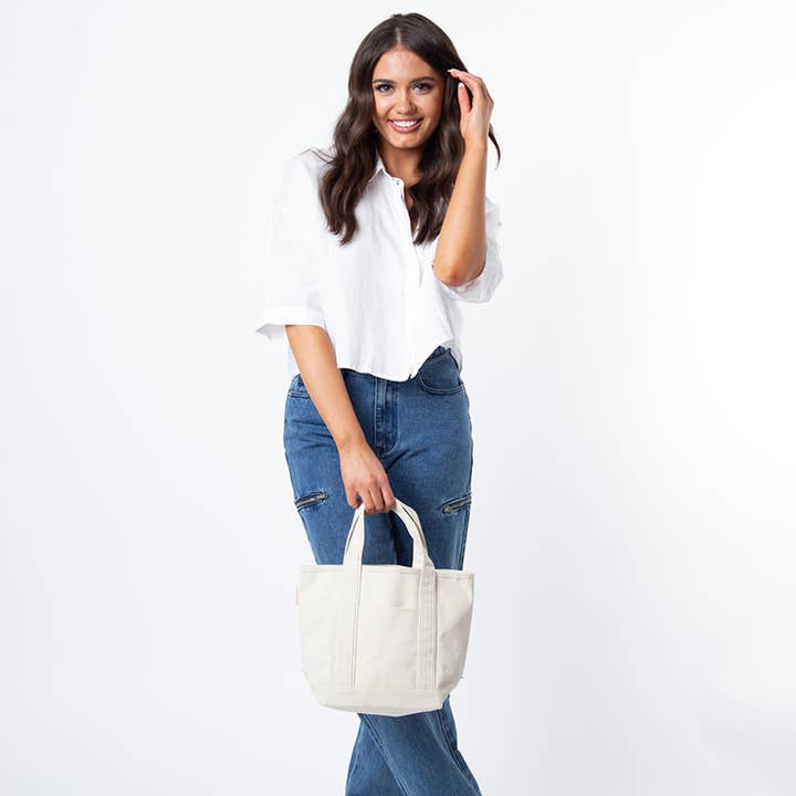 a person wearing jeans and a white top holding the natural tote