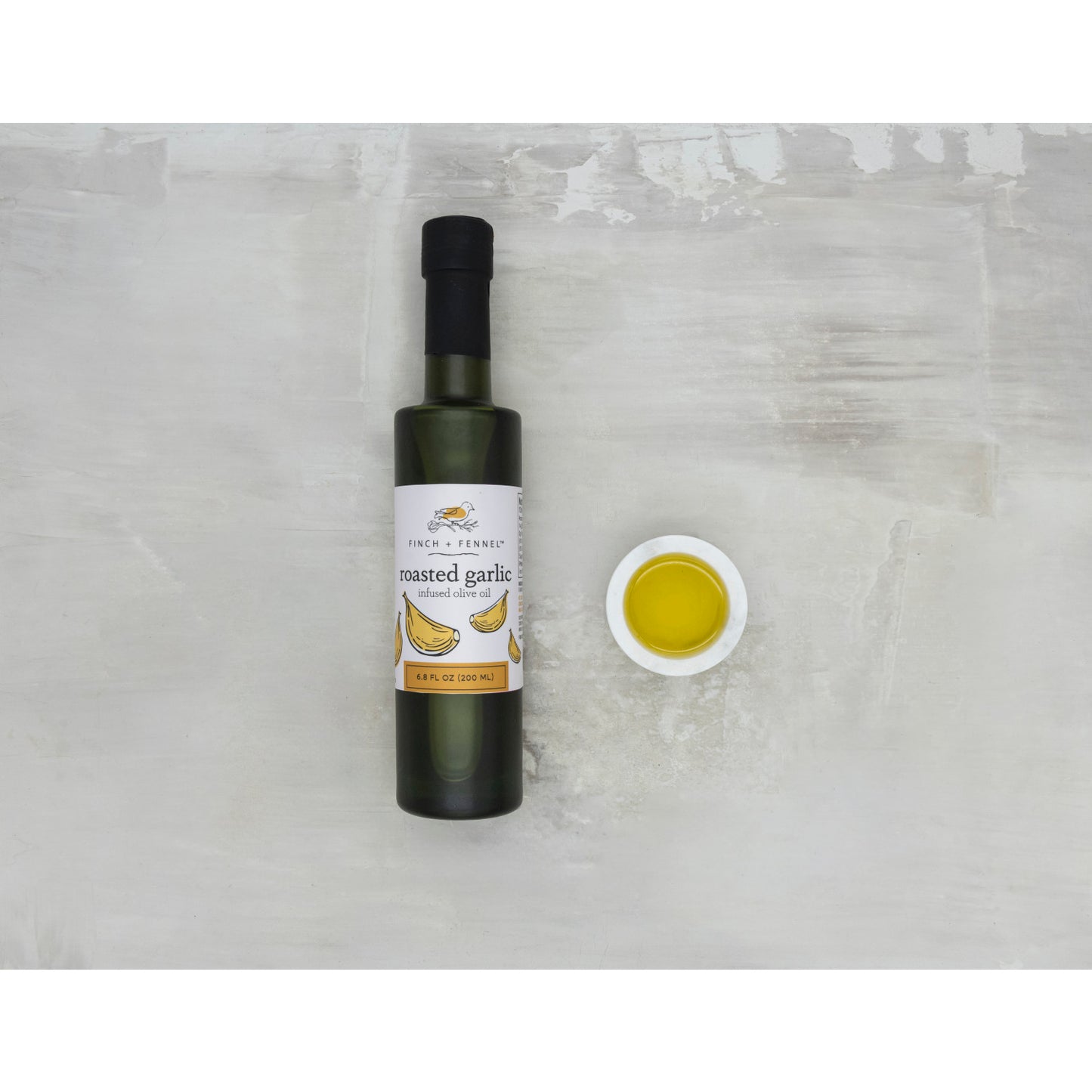 Bottle of roasted garlic oil with a small dish of oil on a light gray background