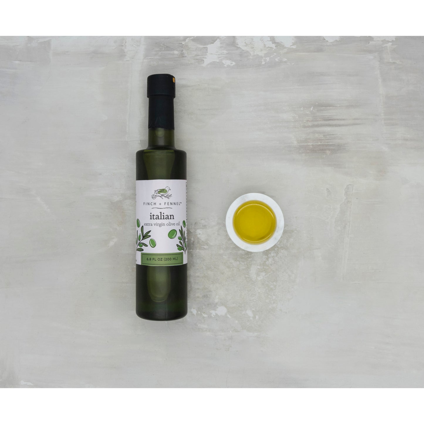 Bottle of Italian olive oil with a small dish of oil on a textured surface