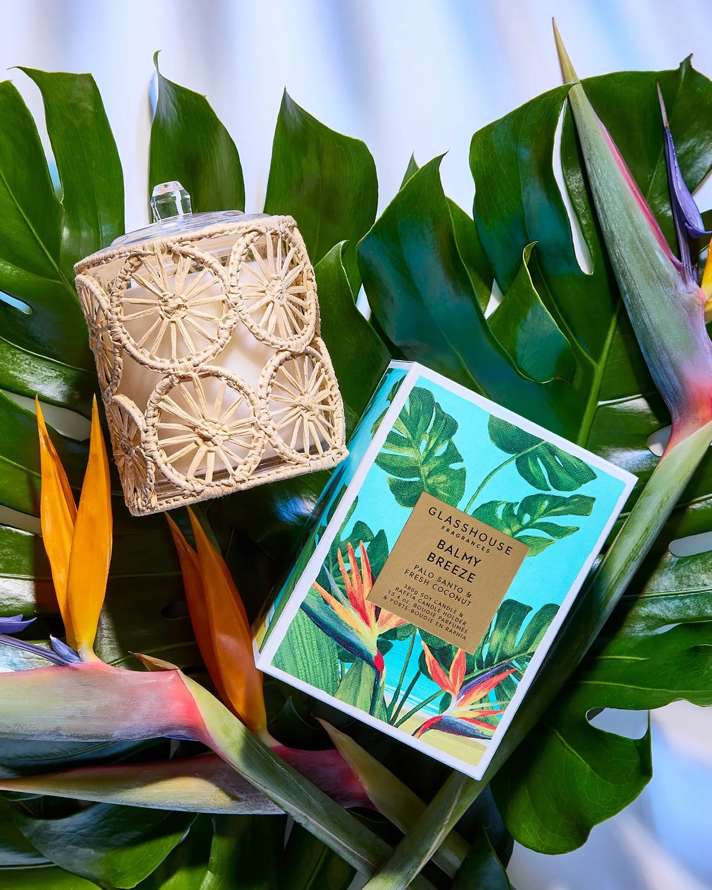 Decorative candle with ratan cover and packaging arranged on tropical leaves