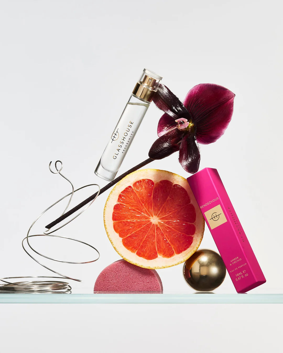 perfume bottle, pink box, orchid flower, and grapefruit arranged artfully on a light background