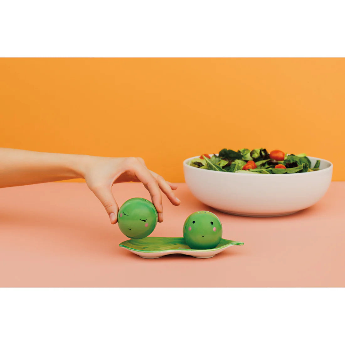pea shakers on a table with a bowl of salad and a hand picking up one of the shakers.