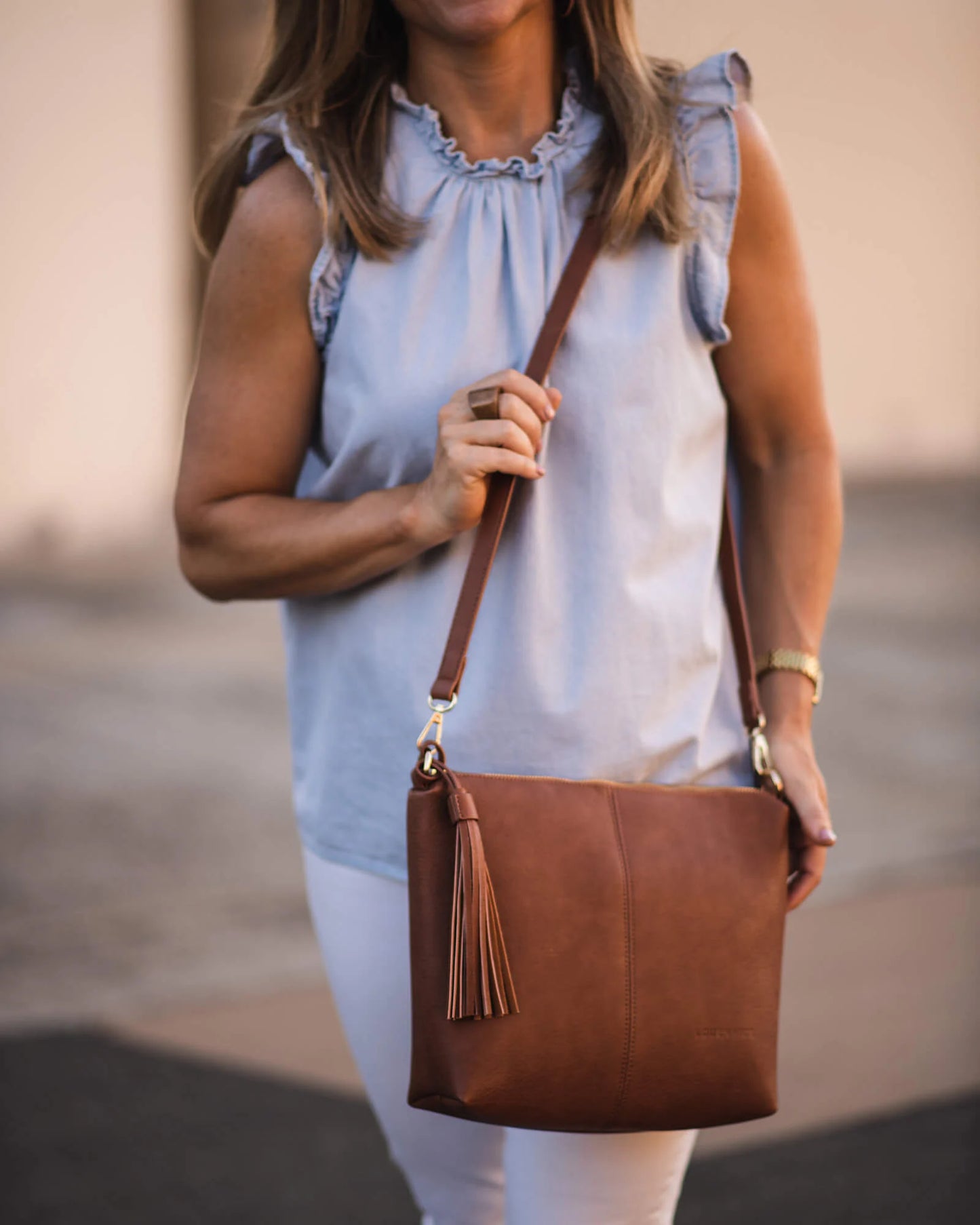 Person wearing light blue blouse with tan Daisy bag on their shoulder.