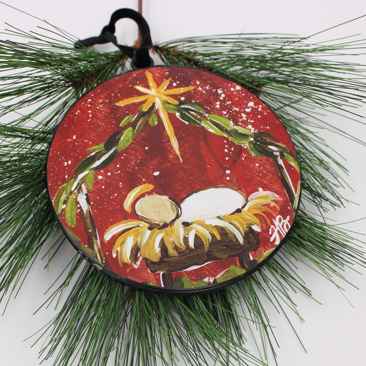 Christmas ornament with a nativity scene laying on a pine branch