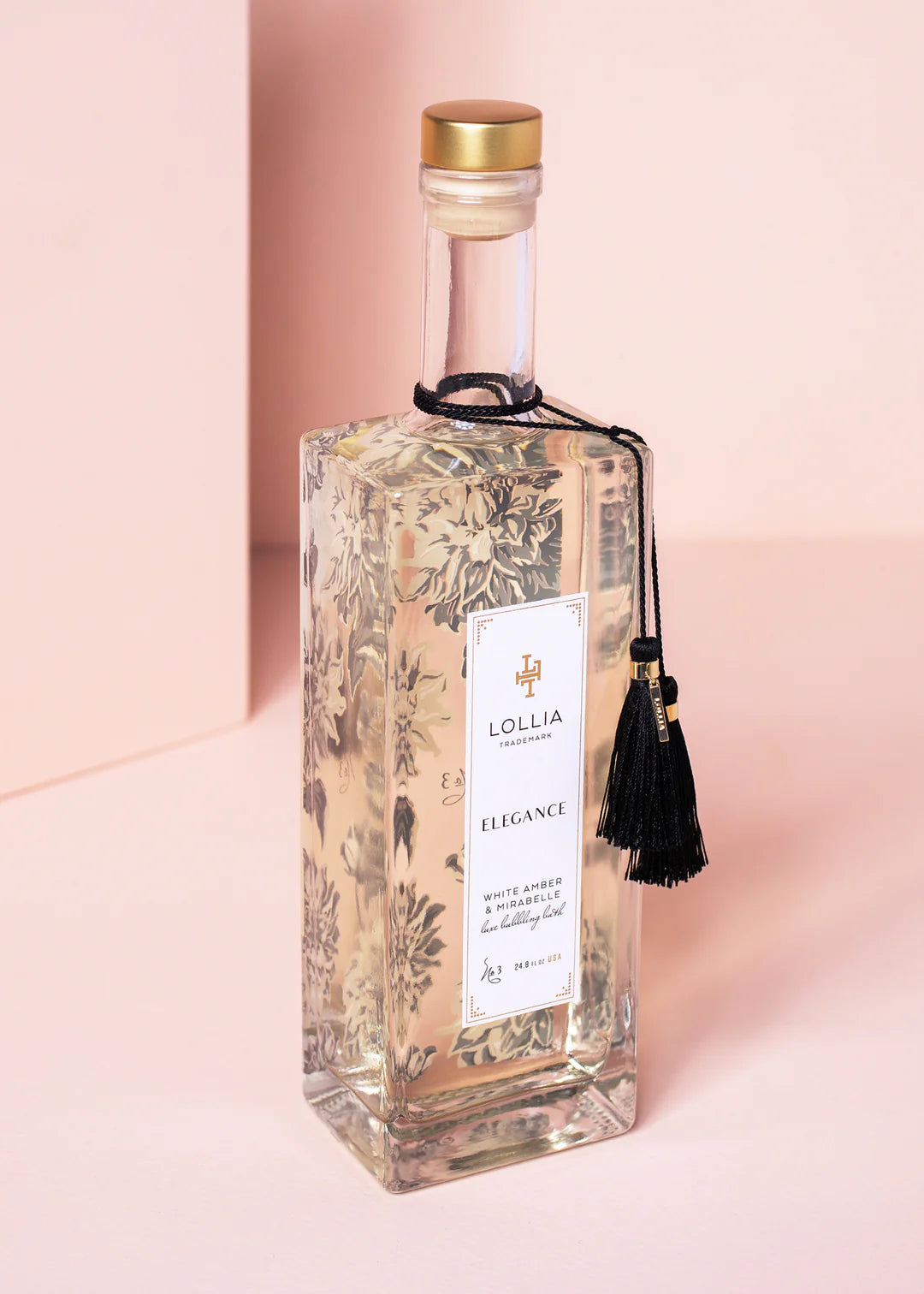 Bottle of elegance bubble bath with black tassels tied around the neck, shone on a pink background.