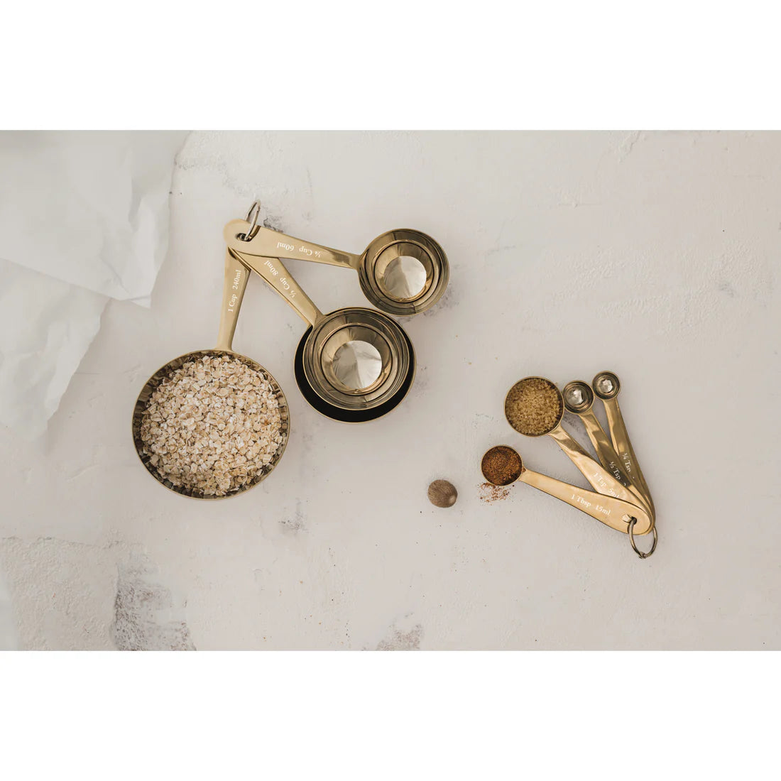 gold measuring cups and spoons arranged on a marble countertop, a few are filled with spices.