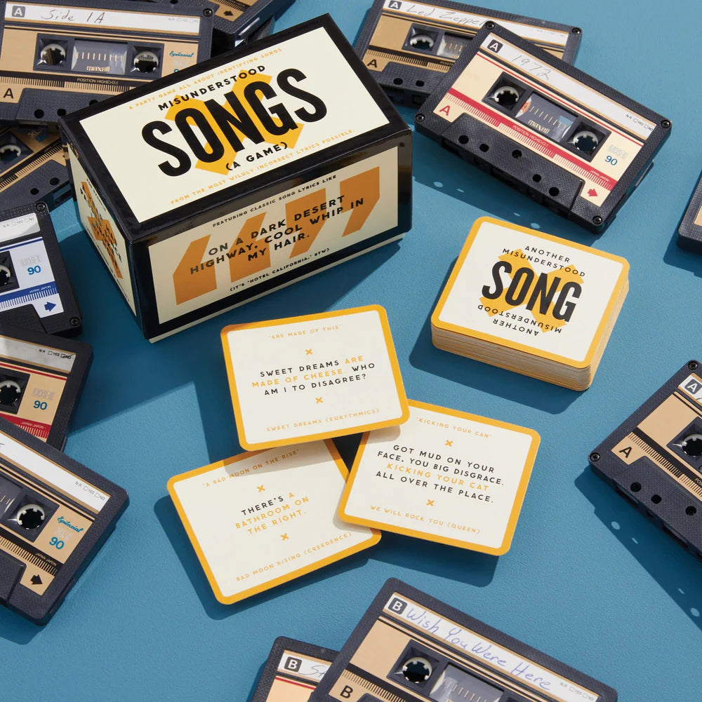 box of misunderstood songs game, cards, and cassette tapes arranged on a blue background.