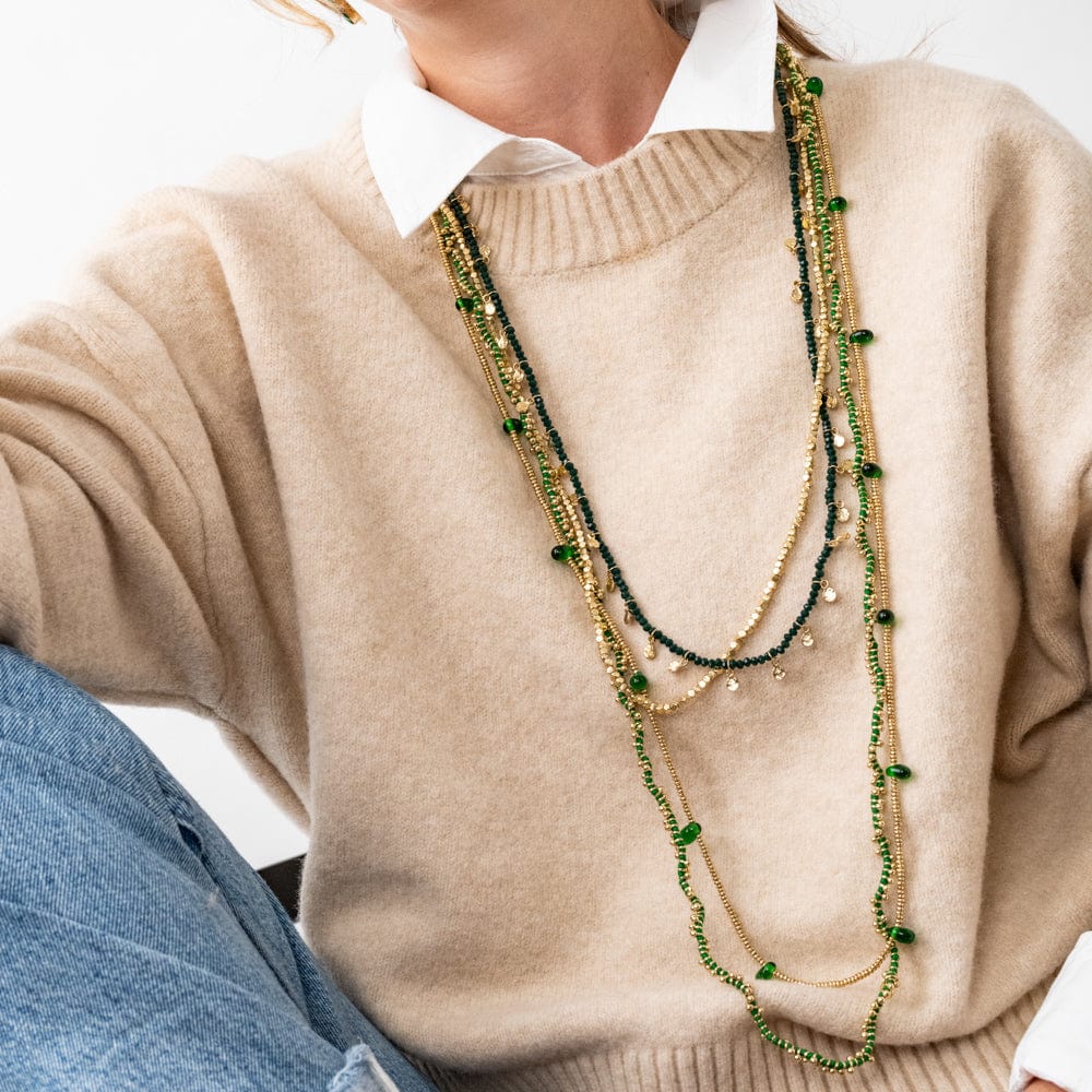 Person wearing a beige sweater with layered green and gold necklaces.