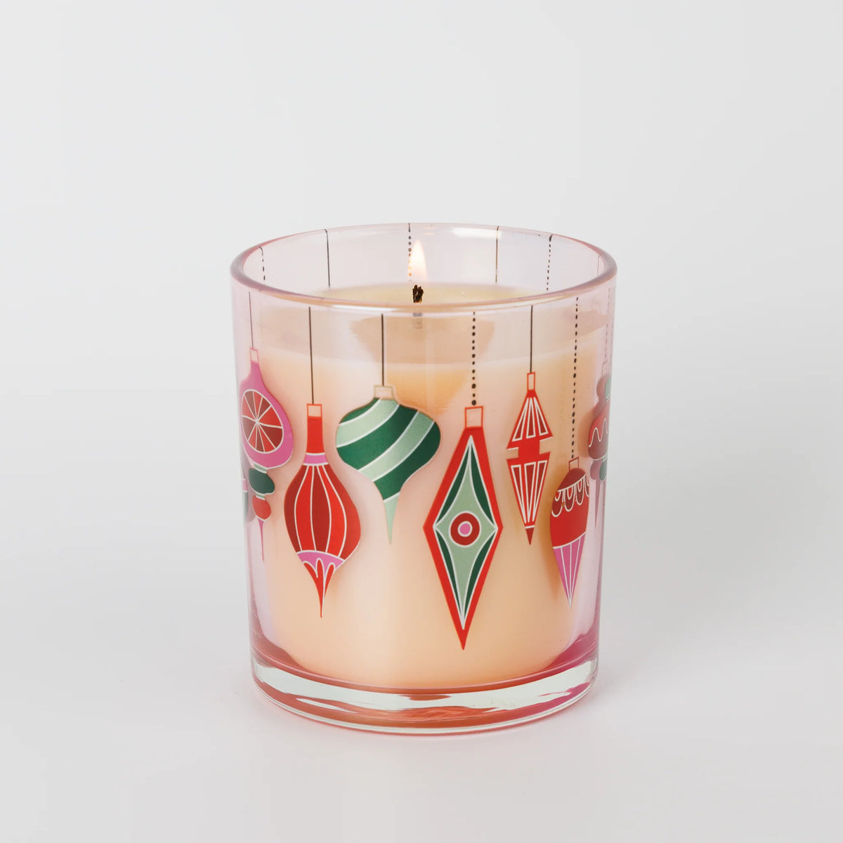 A lit scented candle in a glass jar decorated with colorful hanging ornament illustrations, set against a plain light gray background.