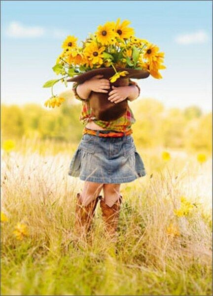 front of card is a little girl in a denim skirt holding a hat full of sunflowers in a grassy field
