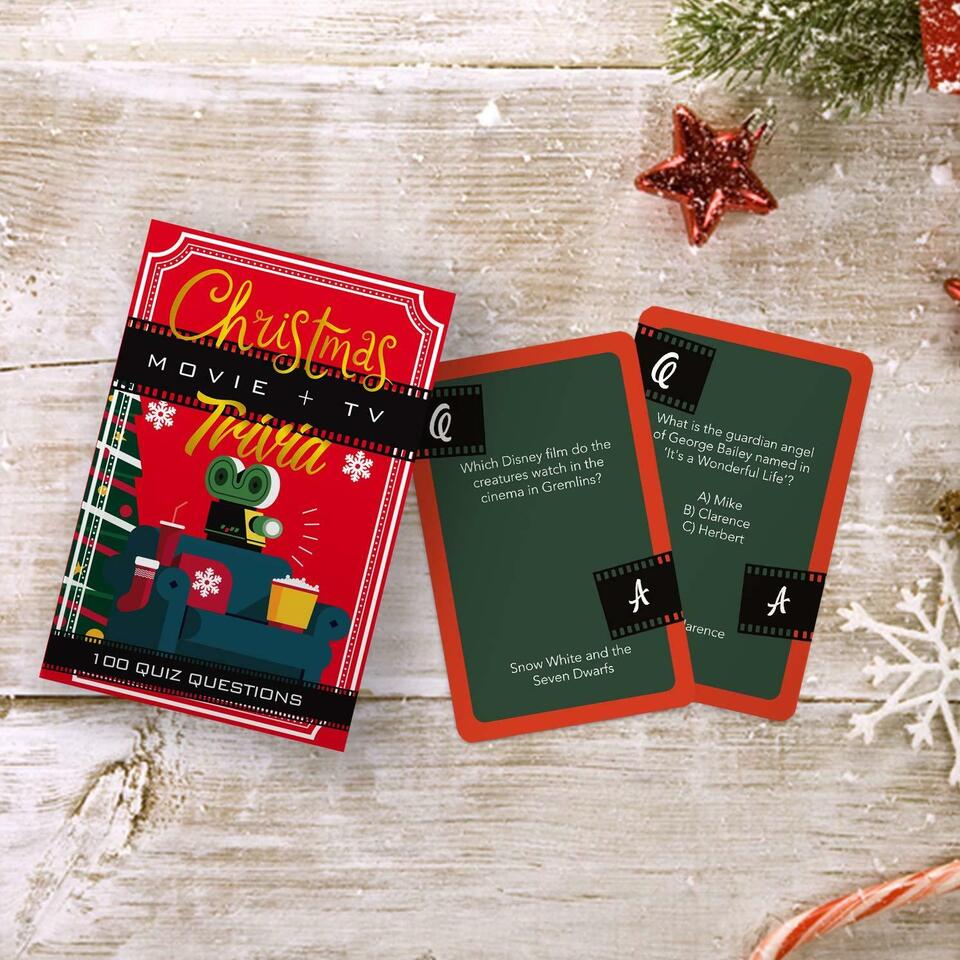 Christmas TV & Movie Trivia cards and box on a wooden table with greenery.