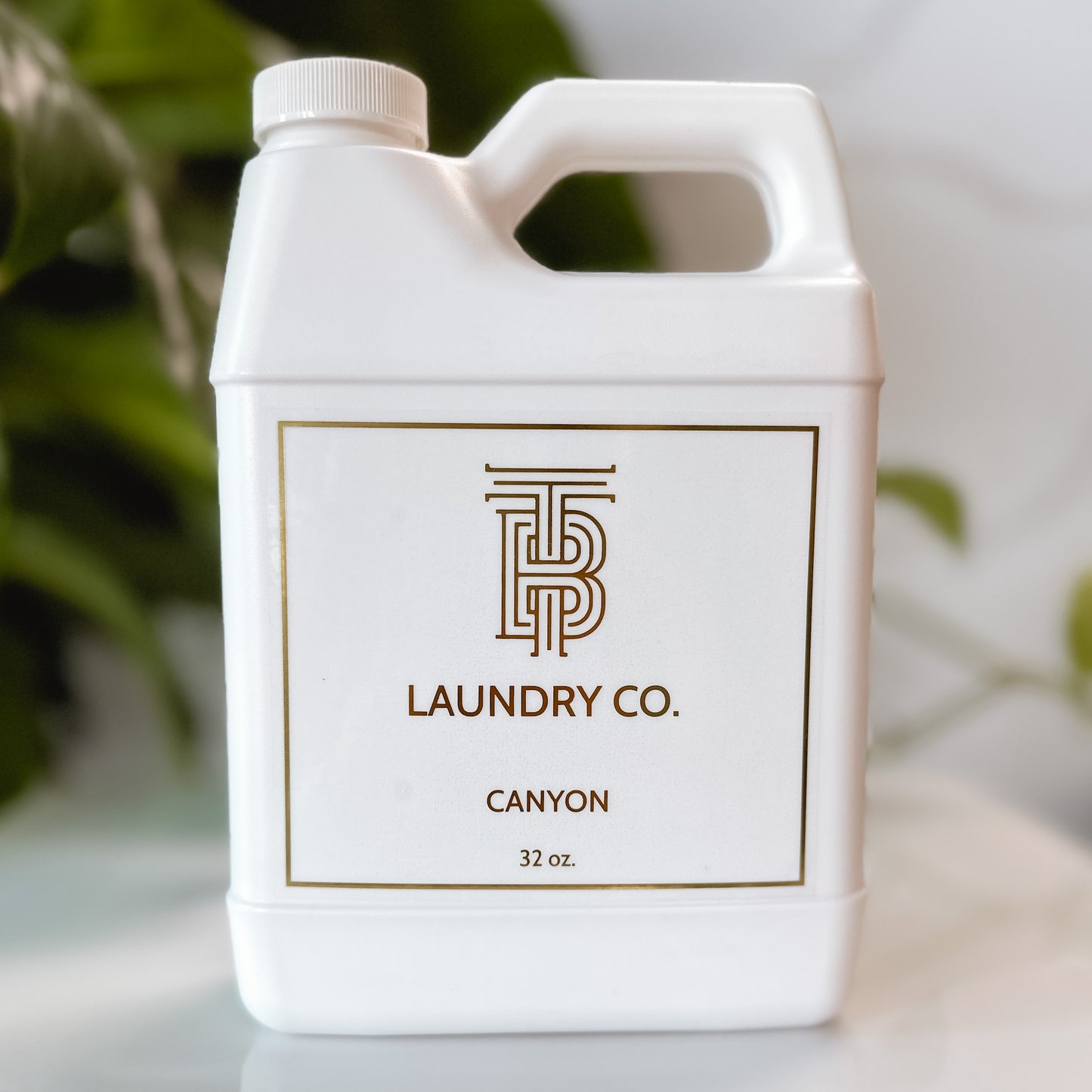 32 ounce plastic bottle of Thomas Blonde Canyon laundry detergent on a white tray and green foliage in the background.