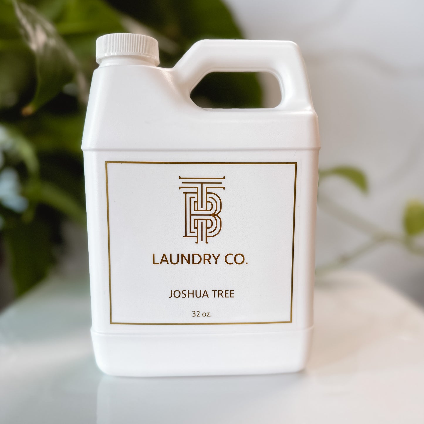 32 ounce plastic bottle of Thomas Blonde Joshua Tree laundry detergent on a white tray with green foliage in the background.
