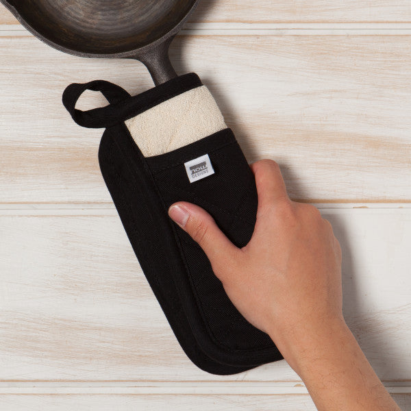 hand using a black potholder to lift a skillet by the handle.