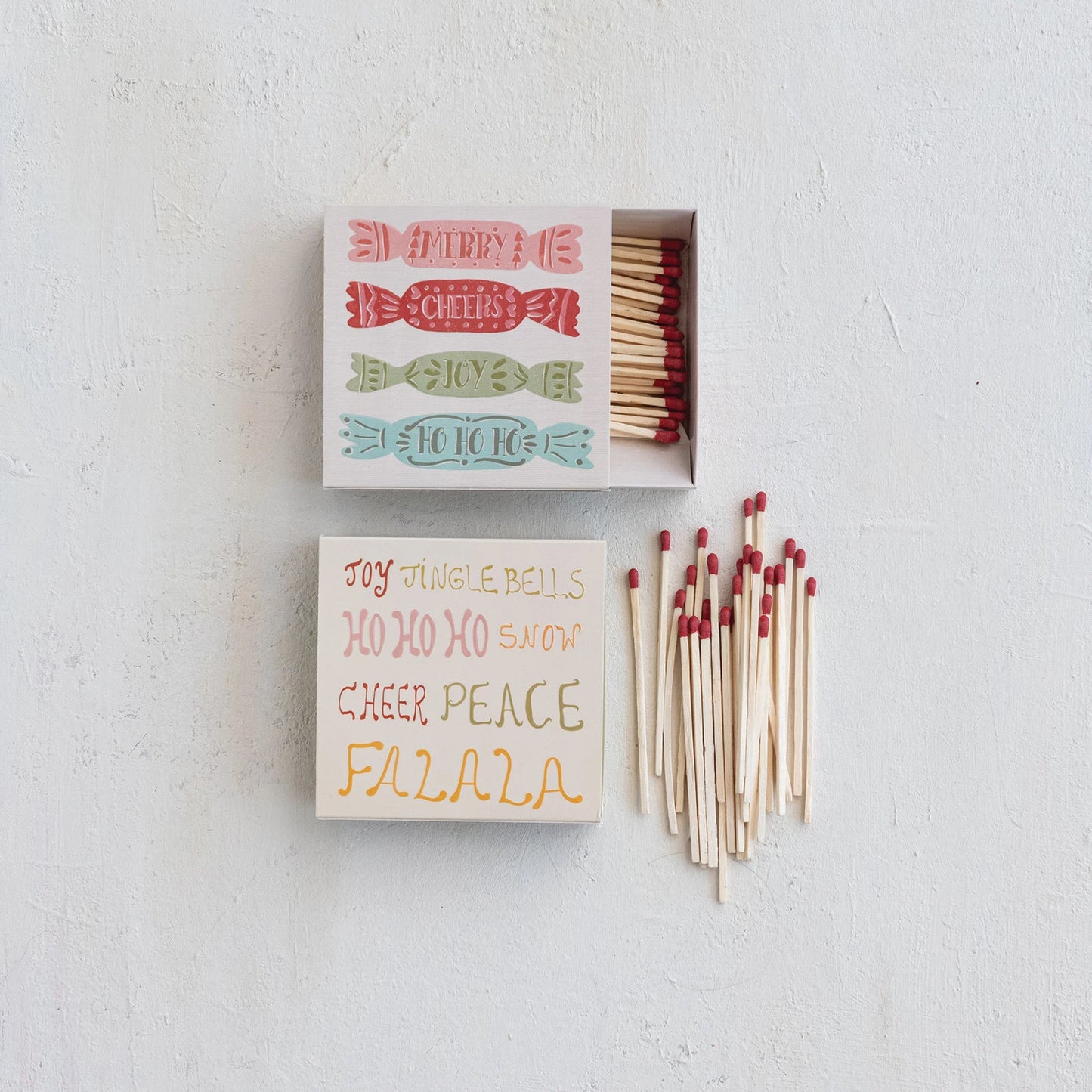 2 styles of Holiday Matches on a table with matches one has candy design, the Christmas words