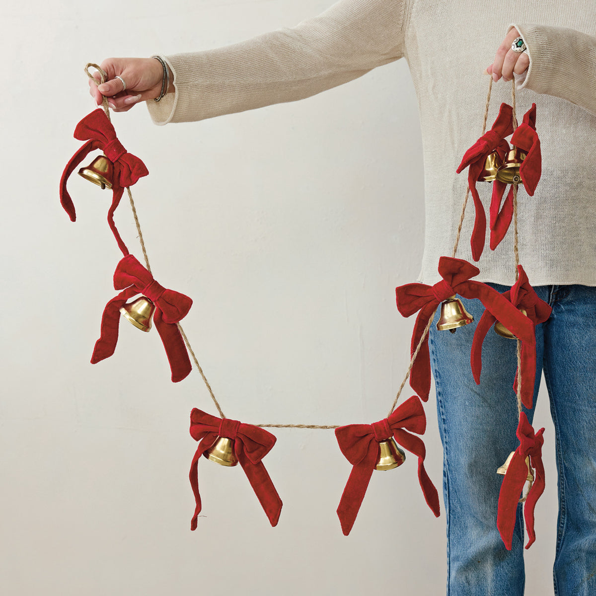 person holding a jute garland of red bows and gold bells