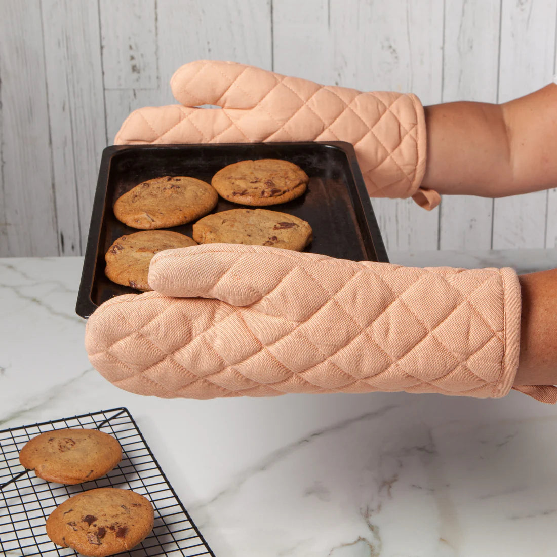 person wearing nectar oven mitts holding a pan of baked cookies.
