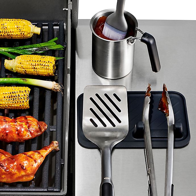 tool rest next to grill with tools on it and food on the grill.