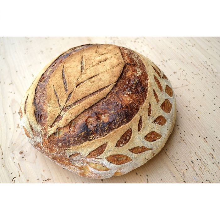 a baked loaf of decoratively scored bread resting on a light wood surface