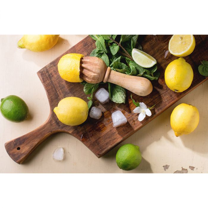 the wooden citrus reamer displayed on a paddle board with lemons limes and mint leaves on a white surface