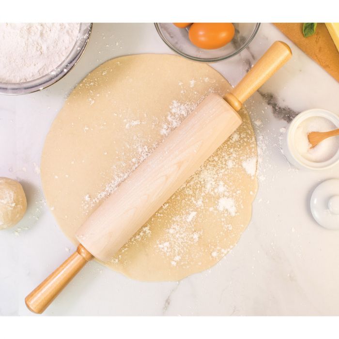 the classic wooden rolling pin displayed on rolled pastry next to a bowl of flower and eggs on a mostly white marble counter