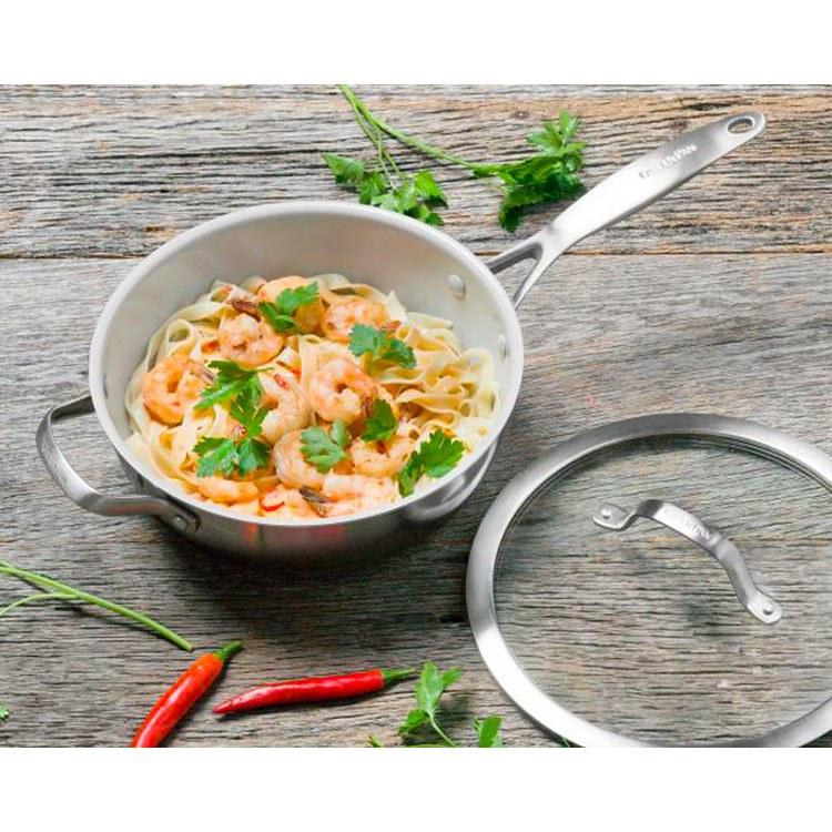 top view of pan filled with pasta and shrimp with lid next to it on wooden table.
