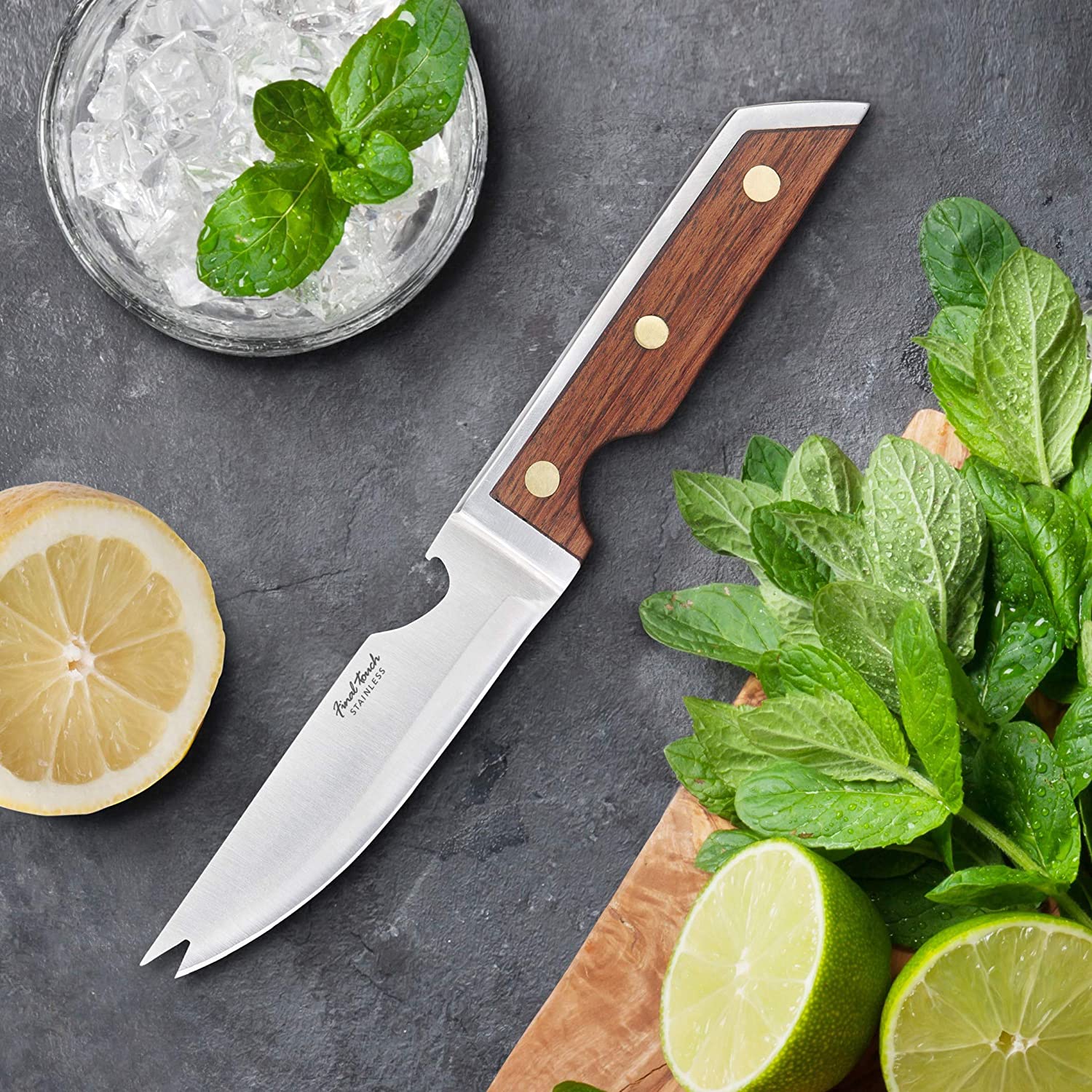 the bartenders bar knife displayed on a piece of slate surrounded by lemon and limes beside a glass of ice