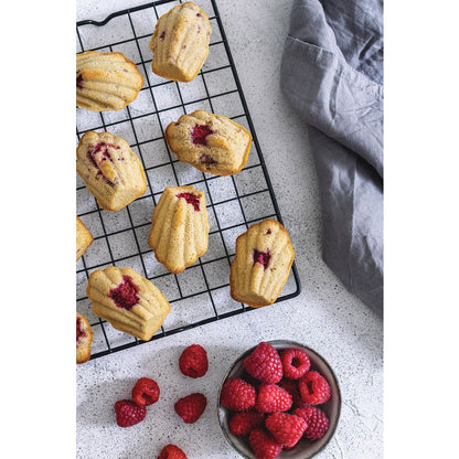 baked madeleines filled with fruit and displayed on a cooling rack next to a bowl of raspberries and towel