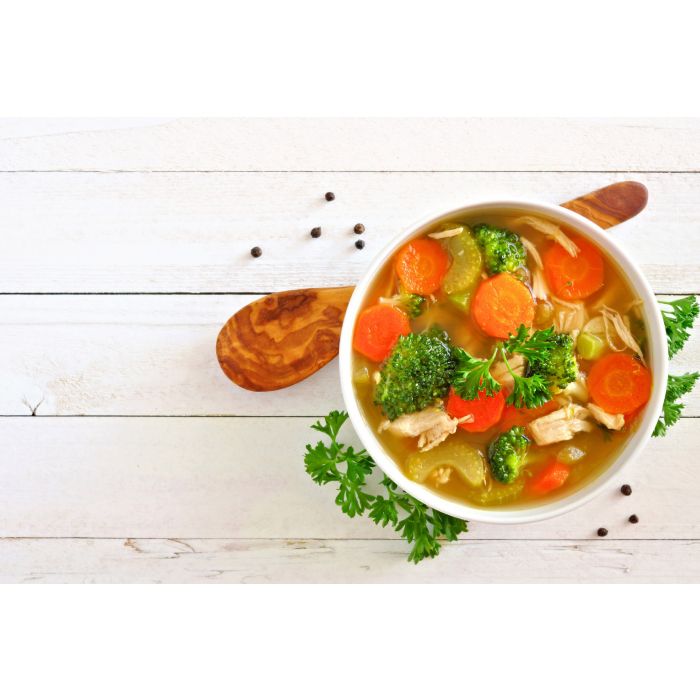 porcelain souffle filled with soup and a wood spoon set next to it on a whitewashed wooden table