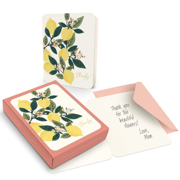 box of cards with a card and envelope outside the box on a white background. cards are off-white with a drawing of a lemon branch with leaves, blossoms, and lemons and says "thanks" in bottom corner. envelopes are blush pink.