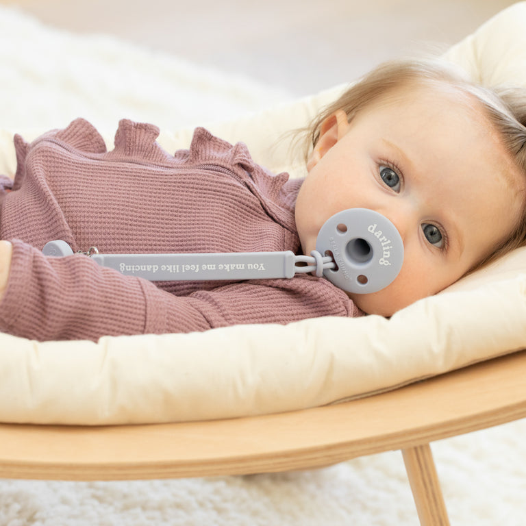 a little girl laying in a wood bouncy seat with the darling bubbi pacifier in her mouth