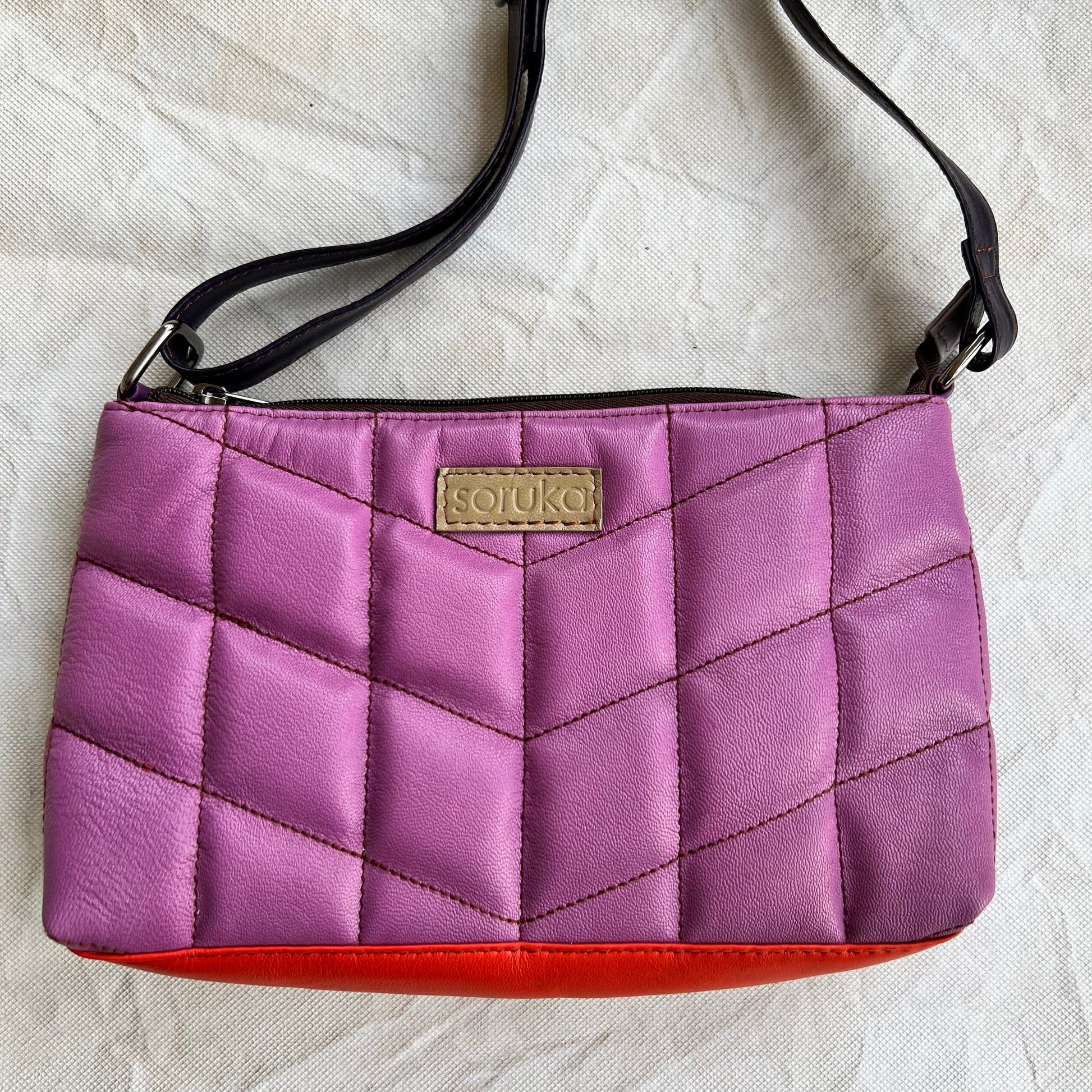 purple puffy quilted leather purse with black  strap and taupe "soruka" logo.