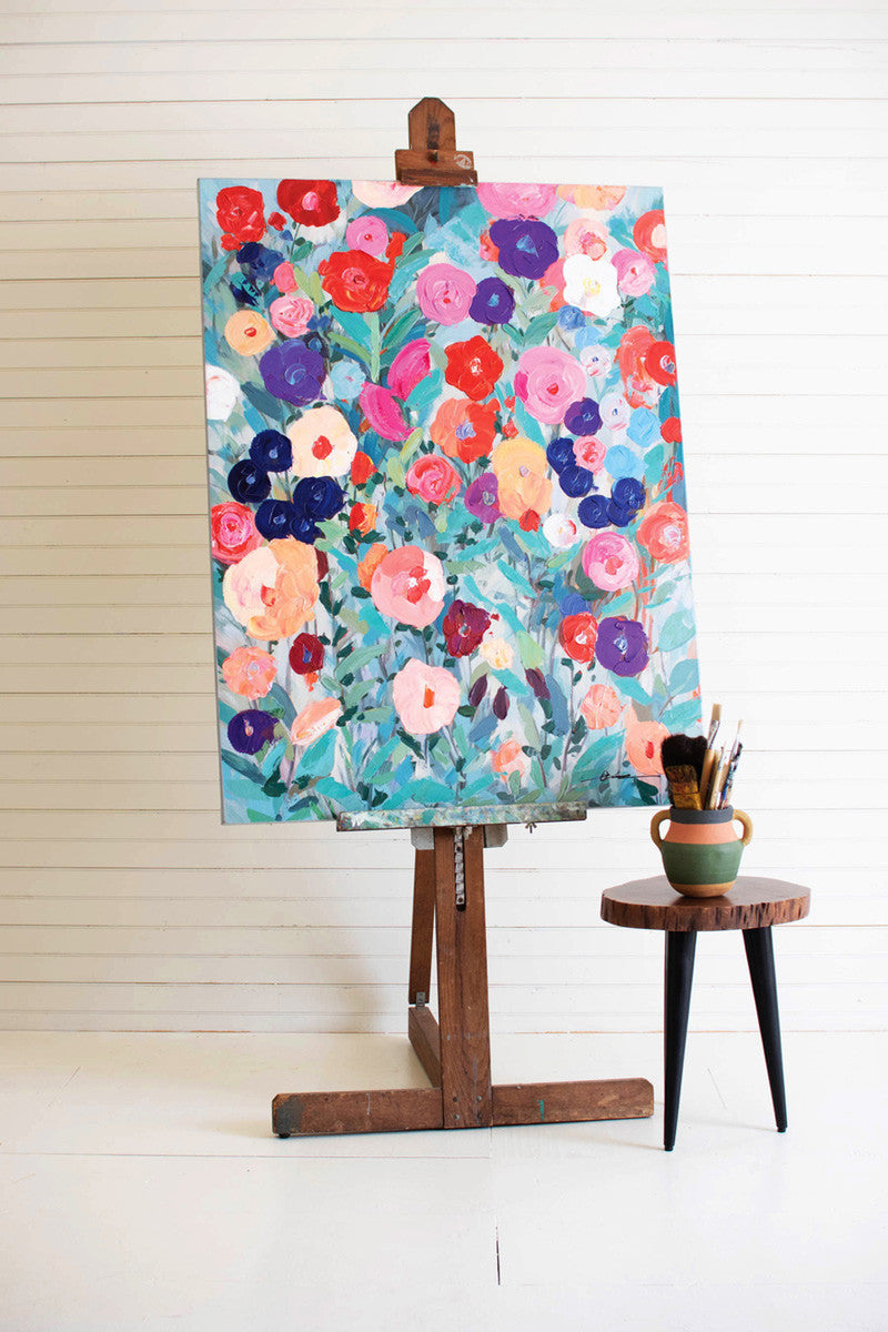 floral painting on an easel with a pot filled with paint brushes next to it,