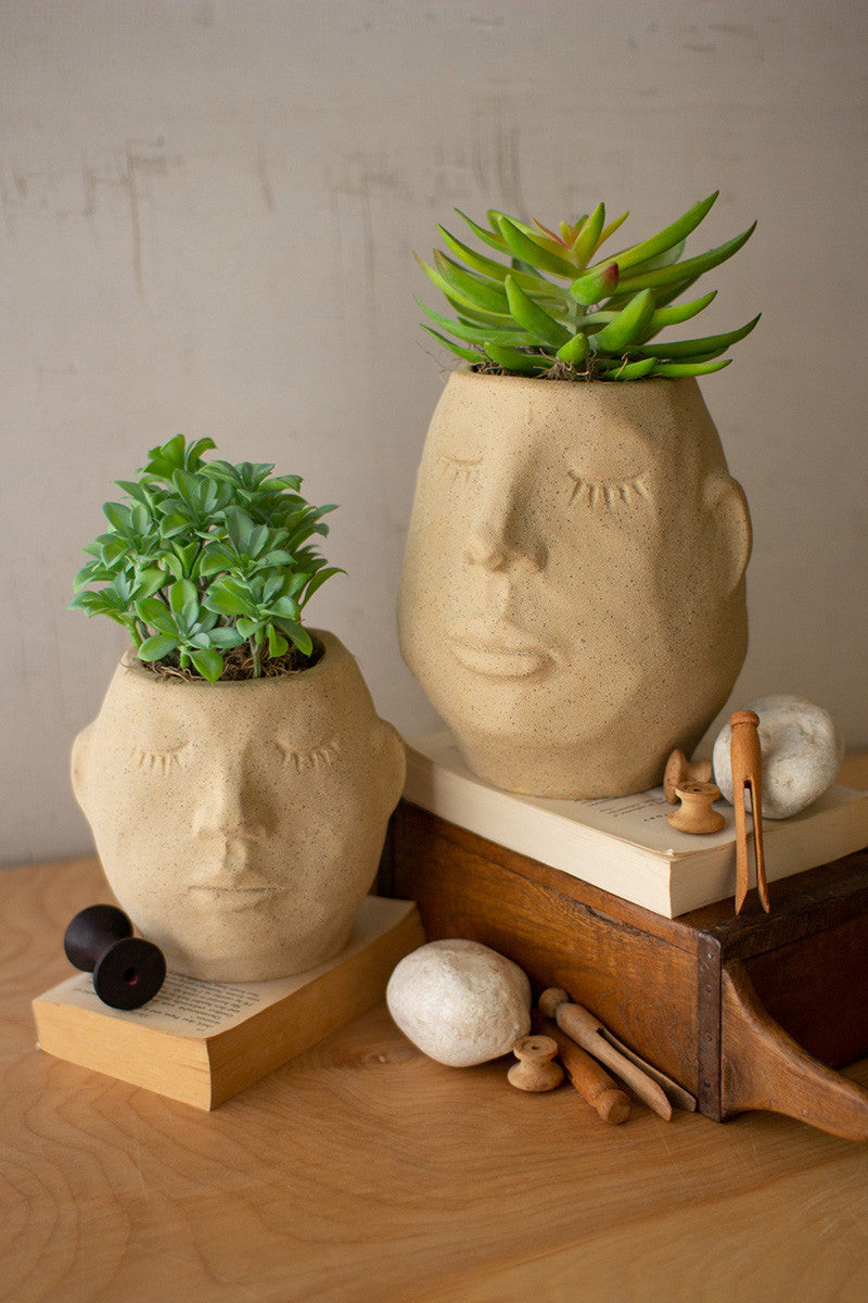 both sizes of ceramic face planters filled with succulents displayed on a book and wooden box on a light wooden surface