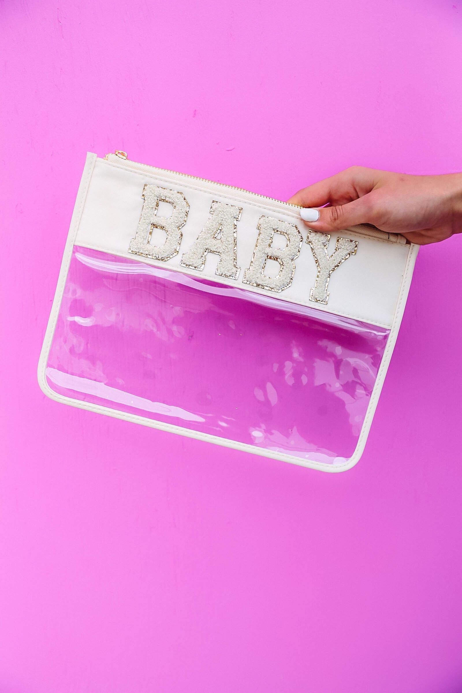 pink background with hand holding clear nylon bag with cream trim and chenille patches that spell "baby".
