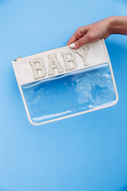 blue background with hand holding clear nylon bag with cream trim and chenille patches that spell "baby".