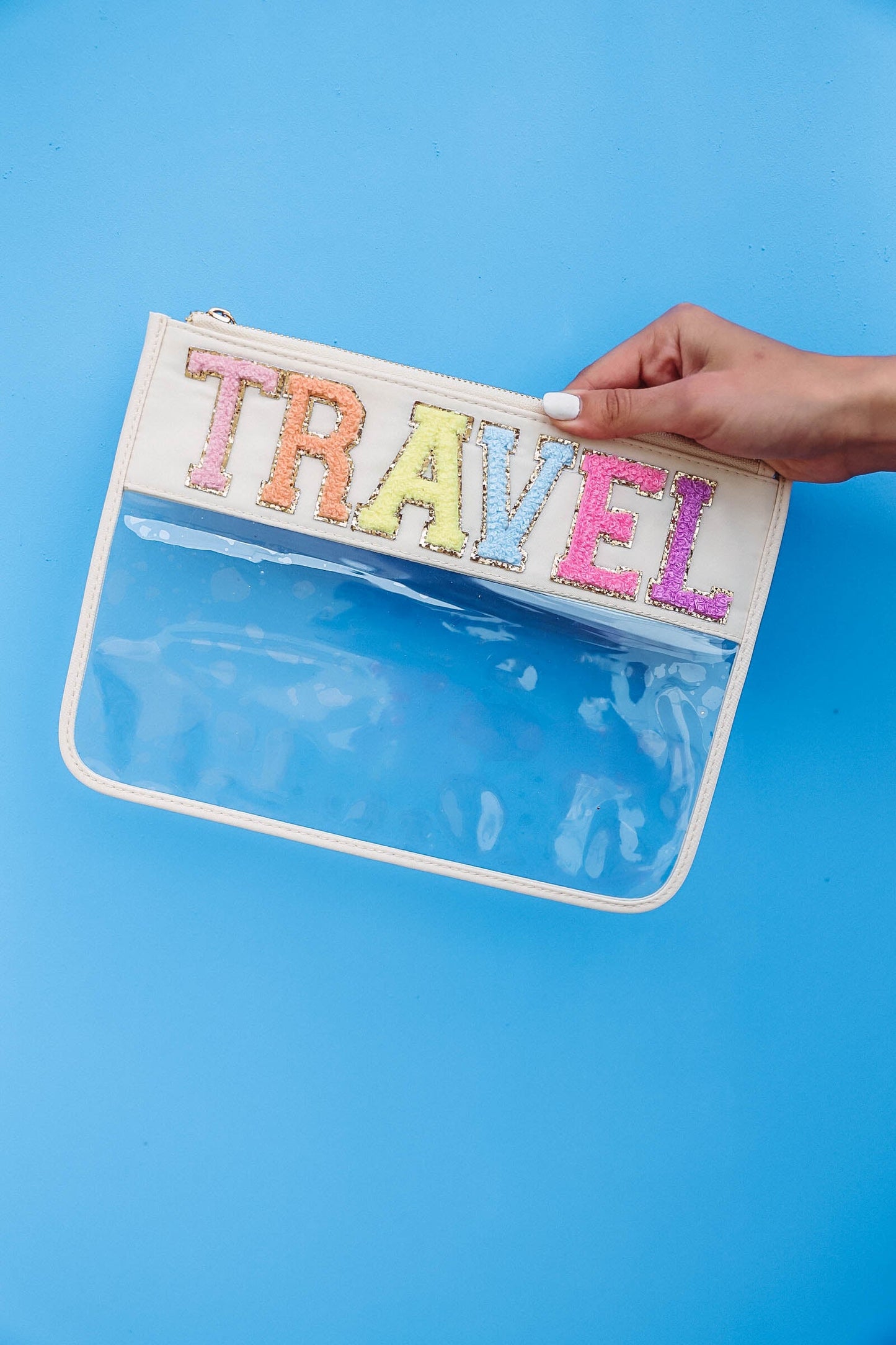 hand holding clear nylon bag with cream trim and chenille patches that spell "travel".